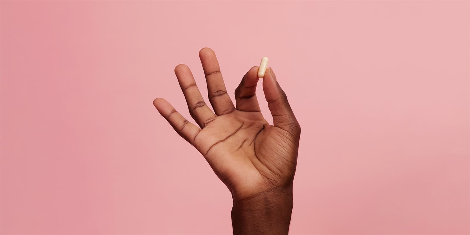 A dark female hand holding up a pill pinched between index finger and thumb