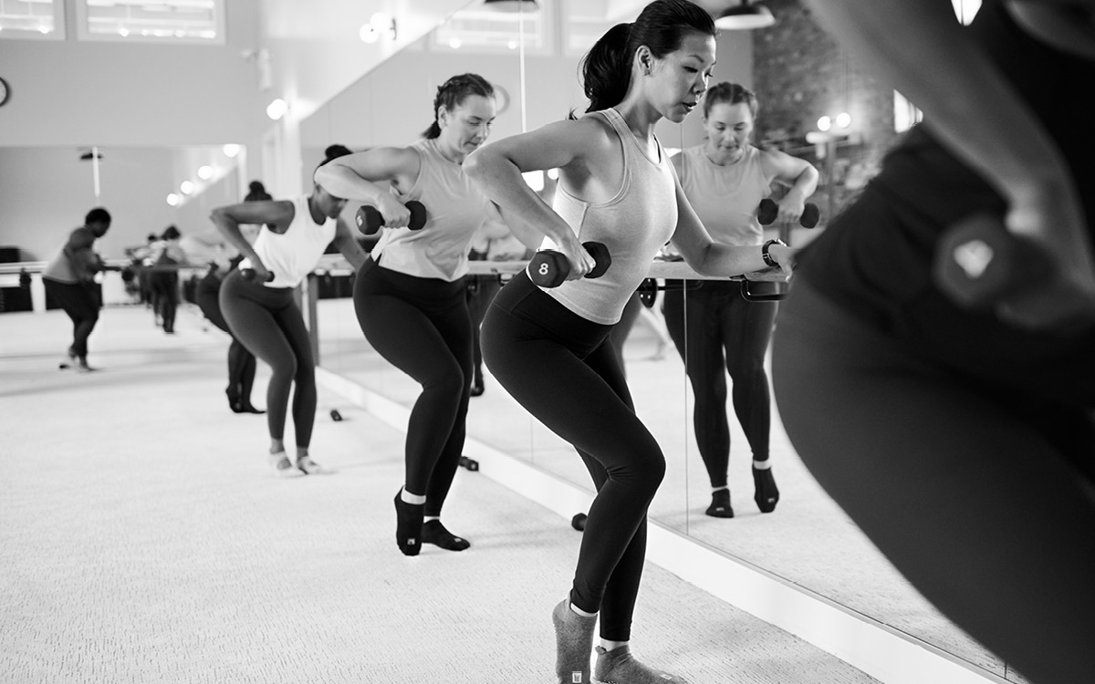 A group fitness class where participants perform bent-over dumbbell rows at the barre, focusing on strength and posture.