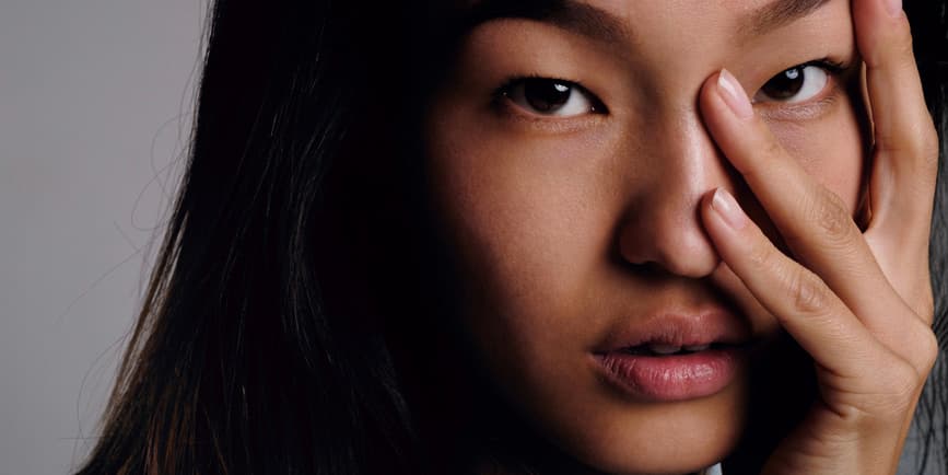 Close-up of calm Korean girl with smooth skin looking at camera with fingers on face.