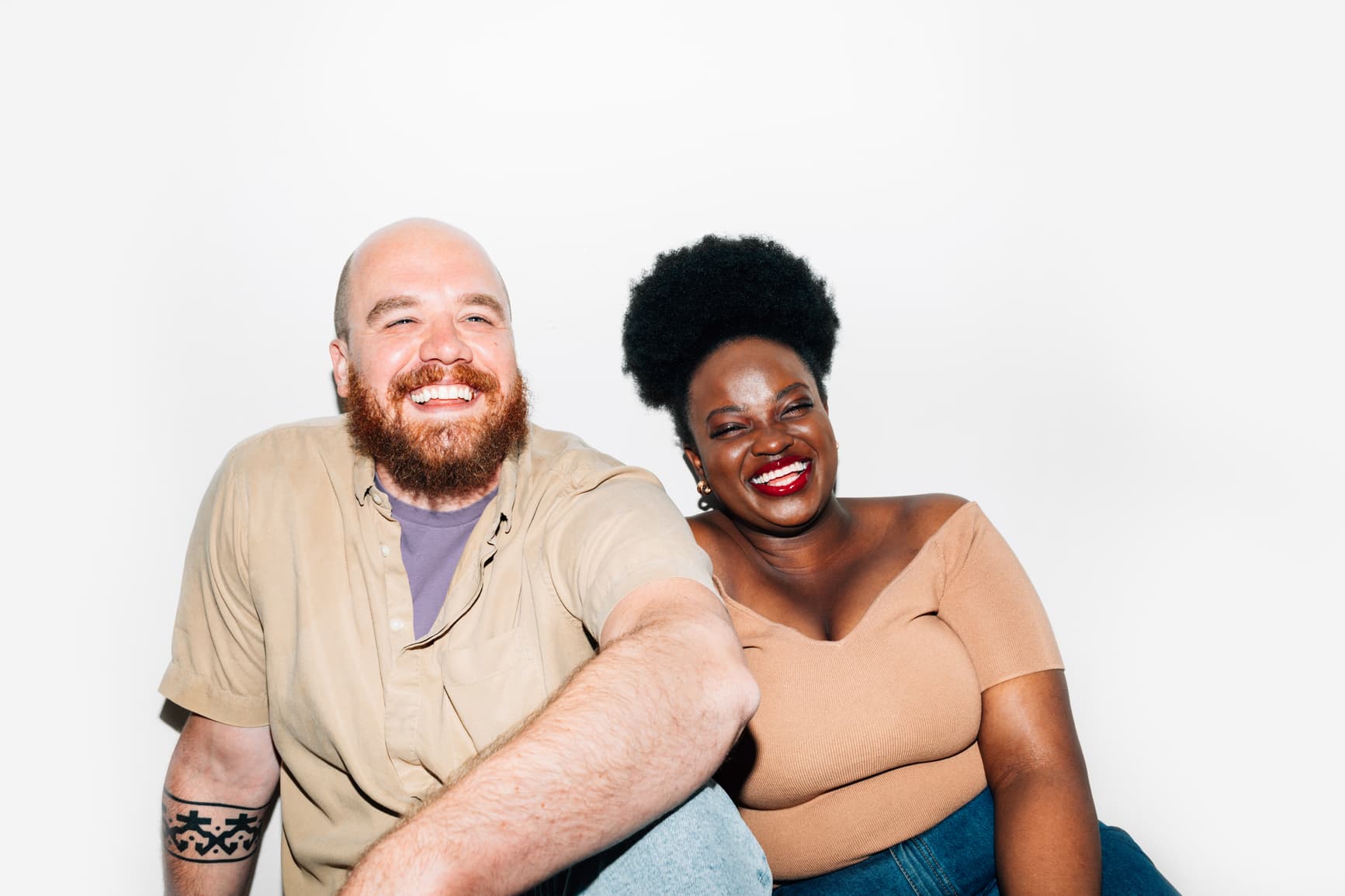 Two people sitting together, laughing and smiling warmly against a white background