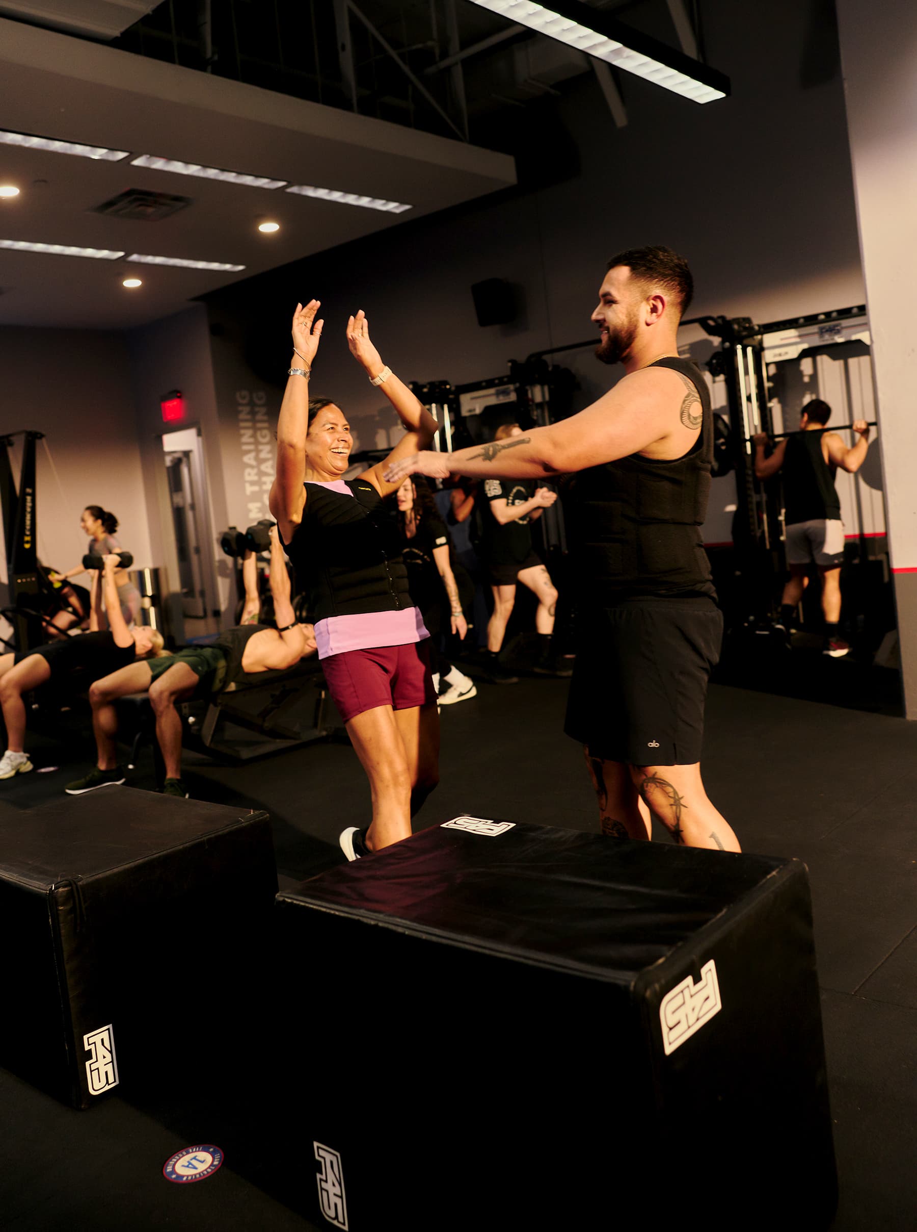 A trainer guides a smiling participant through a workout in a group fitness class