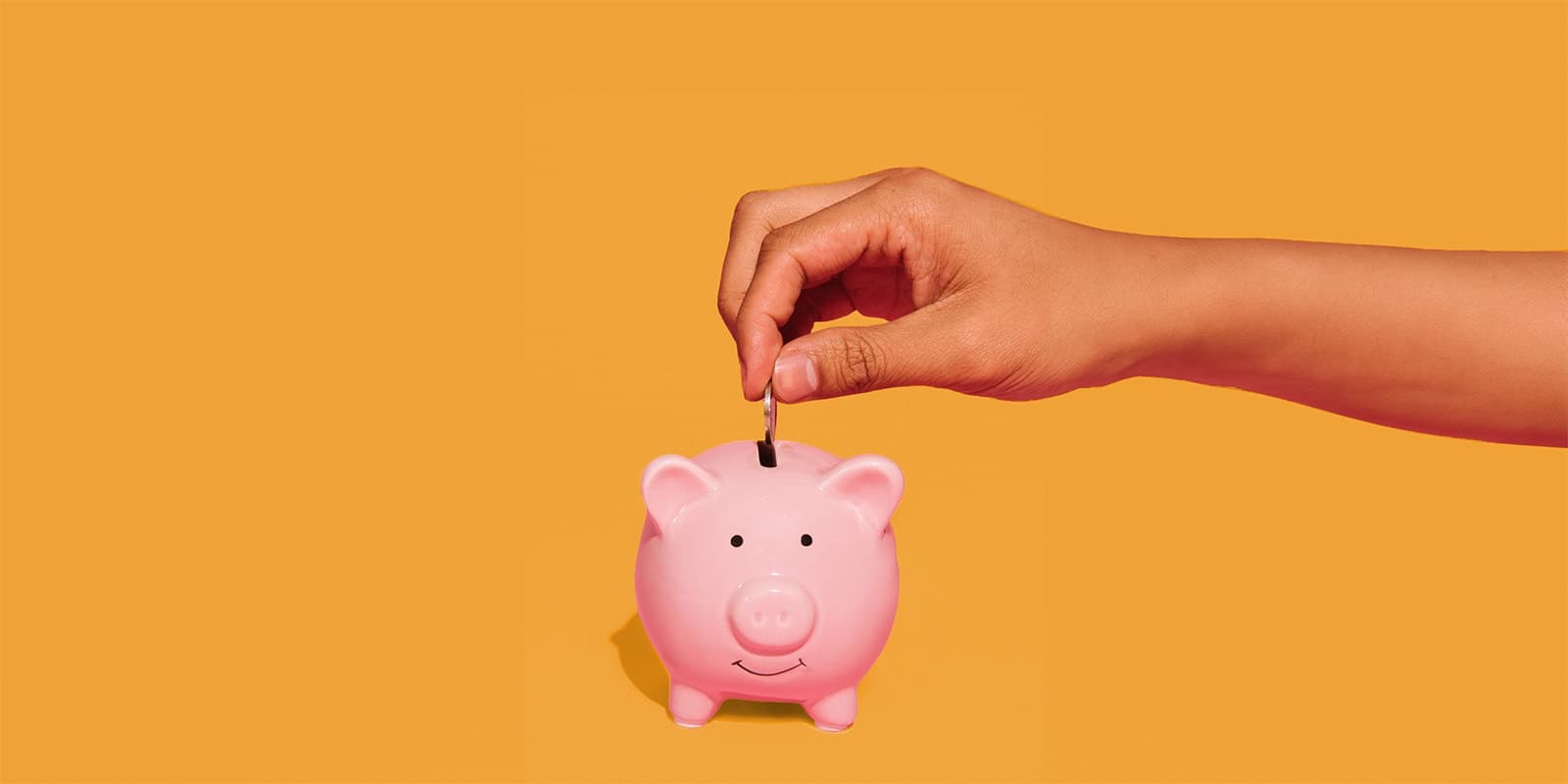 A hand inserting a coin into a piggy bank