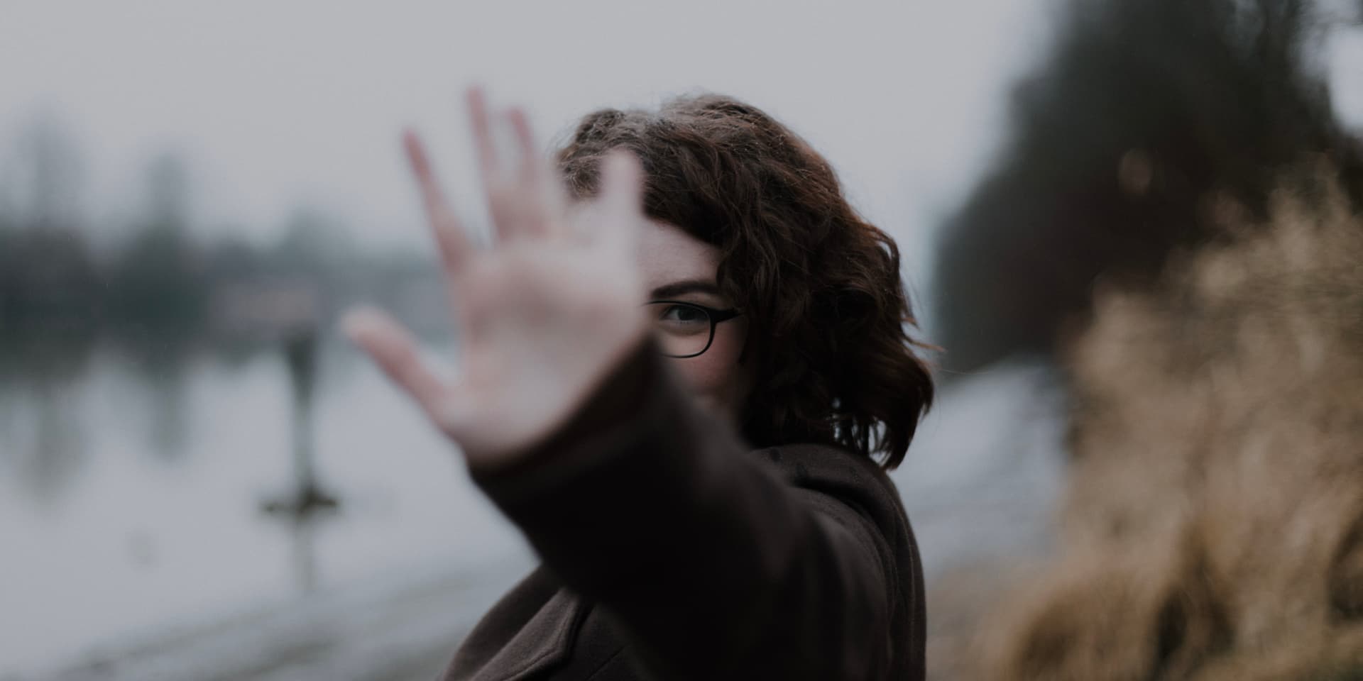 a young white woman with shoulder-length brown hair has an arm outstretched with a gesture that signifies staying away
