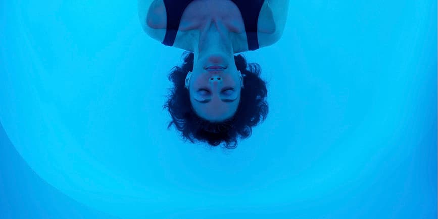 Woman in flotation tank A young white woman floats with her eyes closed in the blue water of a sensory deprivation tank.