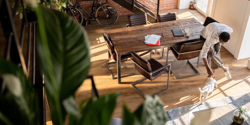 Man and his dog at home View from above of a young Black man caressing his dog in a spacious, stylish living room. There is notebook and folder with documents on the table.