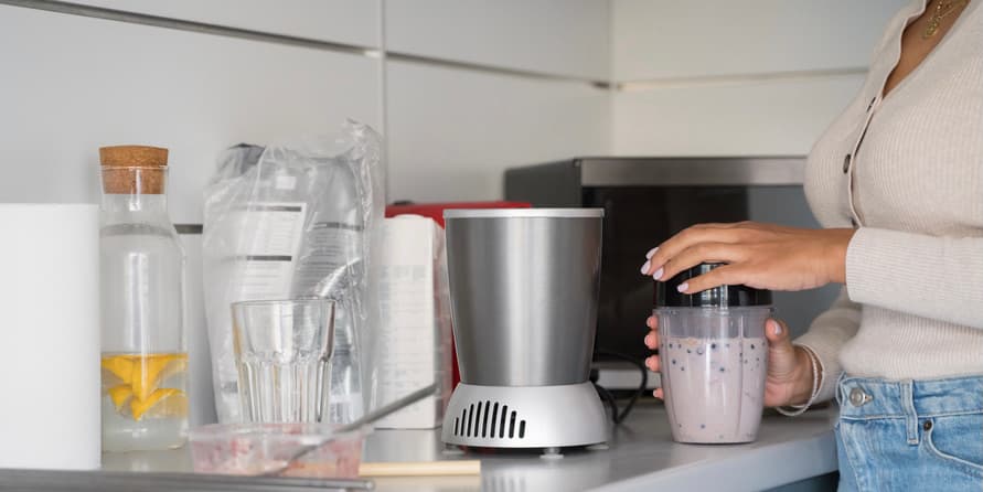 Woman making smoothie Close up photo of a woman with brown skin wearing a tan shirt preparing a breakfast smoothie.