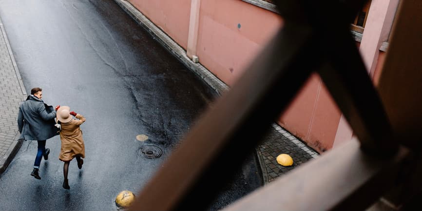 Couple running in a road A long photo taken above of a white man and woman in warm stylish clothes holding hands and running on the road in a city.
