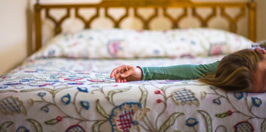 The head and arm of a white woman lying on a colorful bedspread is shown to the side of the photograph. She is lying face down, and looks like she's in pain.