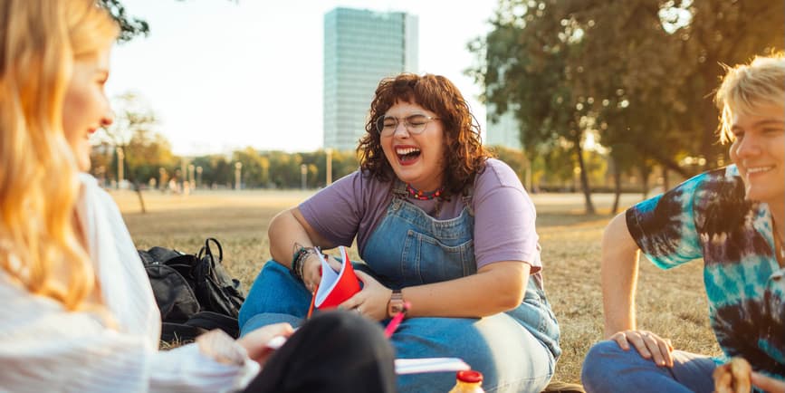 Friends in a park Two beautiful young curvy white women and a young white man sitting in park have a picnic, laughing together.