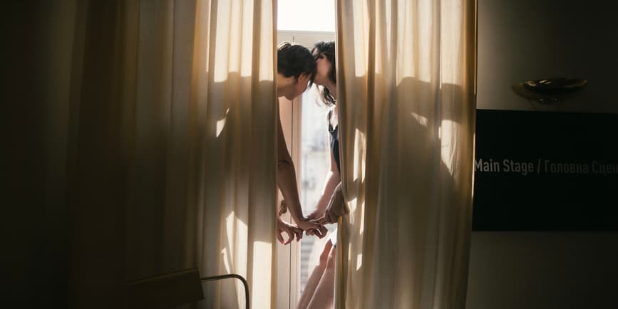Women embracing behind curtains A young lesbian couple reaches toward each other behind gauzy curtains with light coming in from doors behind them.