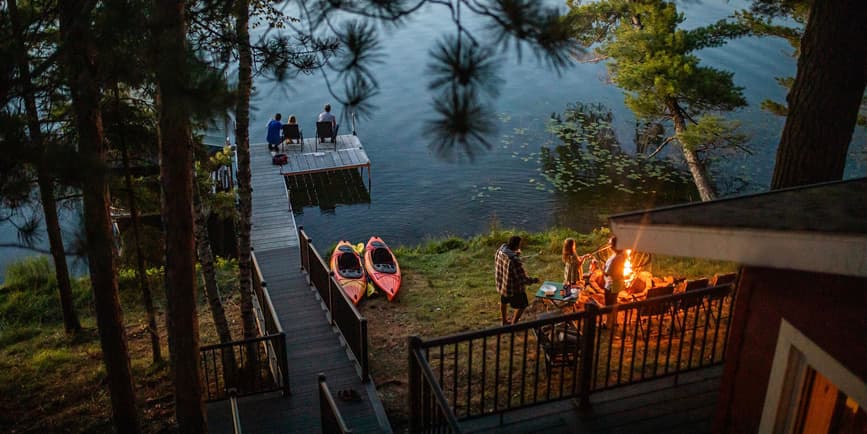 Grandpa and granddaughter fish off the end of a dock and family has a bonfire on a beautiful summer evening.