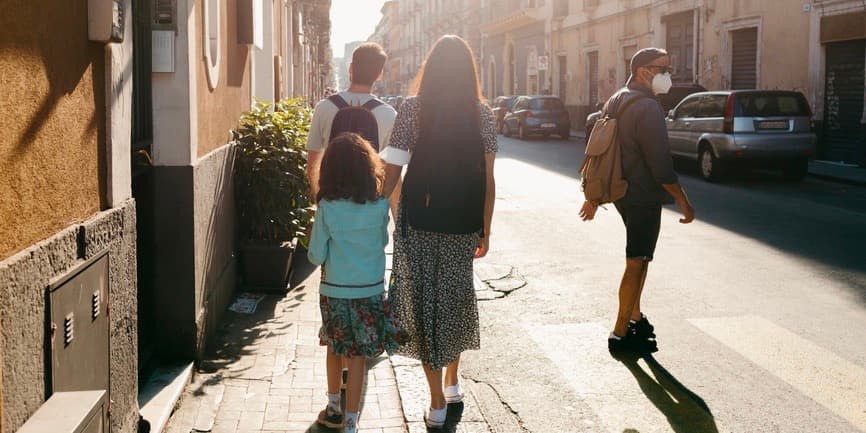 Family walking in Italy. Group of tourist family walking on the narrow sidewalk of old Italian city of Catania in sunny day. View from the back.