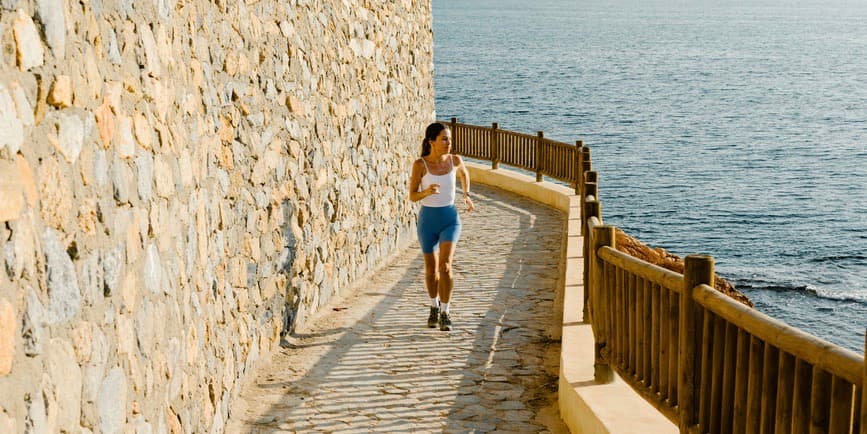 Woman jogging by sea. A young lady jogs along a boardwalk early in the morning during her vacation by the Mediterranean Sea, enjoying the sunny weather.
