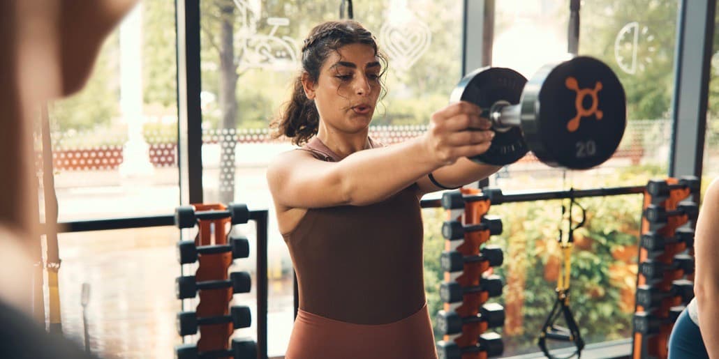 A young woman concentrates as she lifts a heavy weight during an Orangtheory Fitness class.