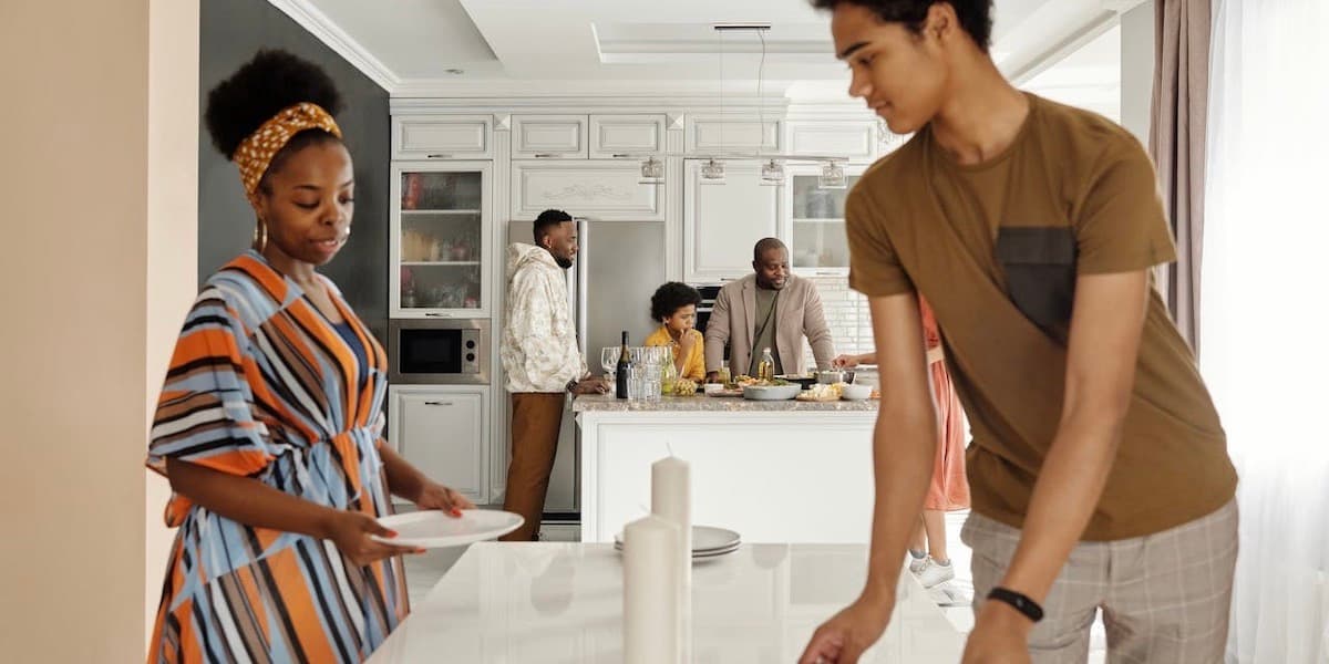 Family cooking and setting table for dinner A Black family in dress clothes prepares dinner and sets the table in a clean, modern, expansive white kitchen and dining room.