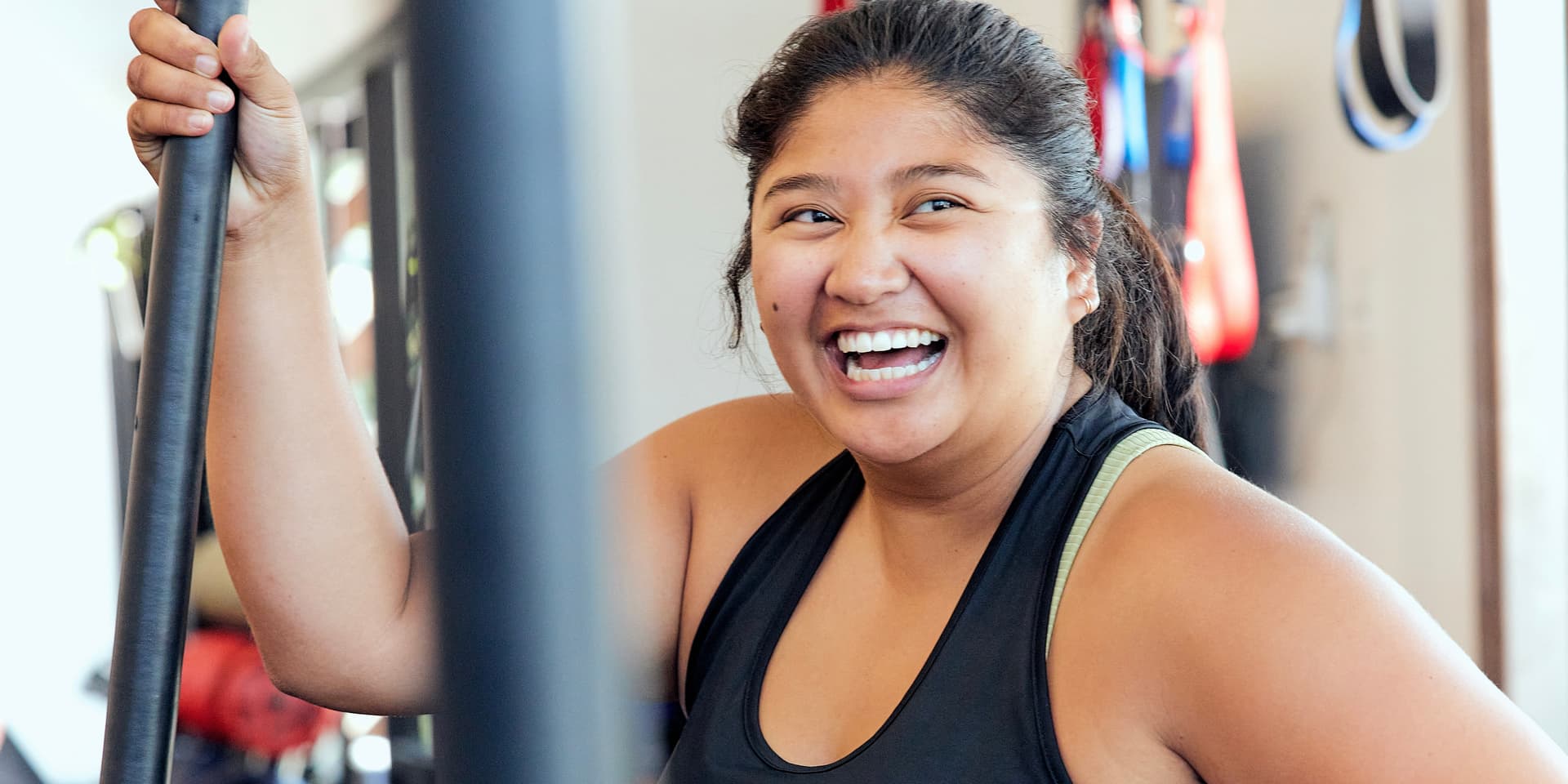 A woman with brown skin and hair smiles as she works out in an F45 Training center.