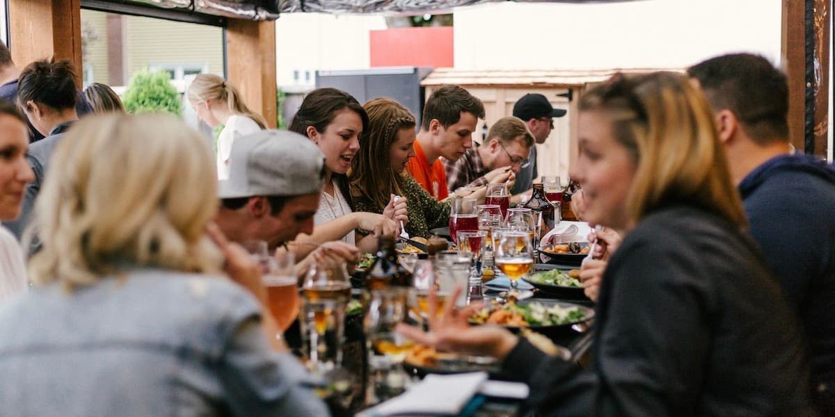 A communal table outside at a restaurant packed with people talking and eating.