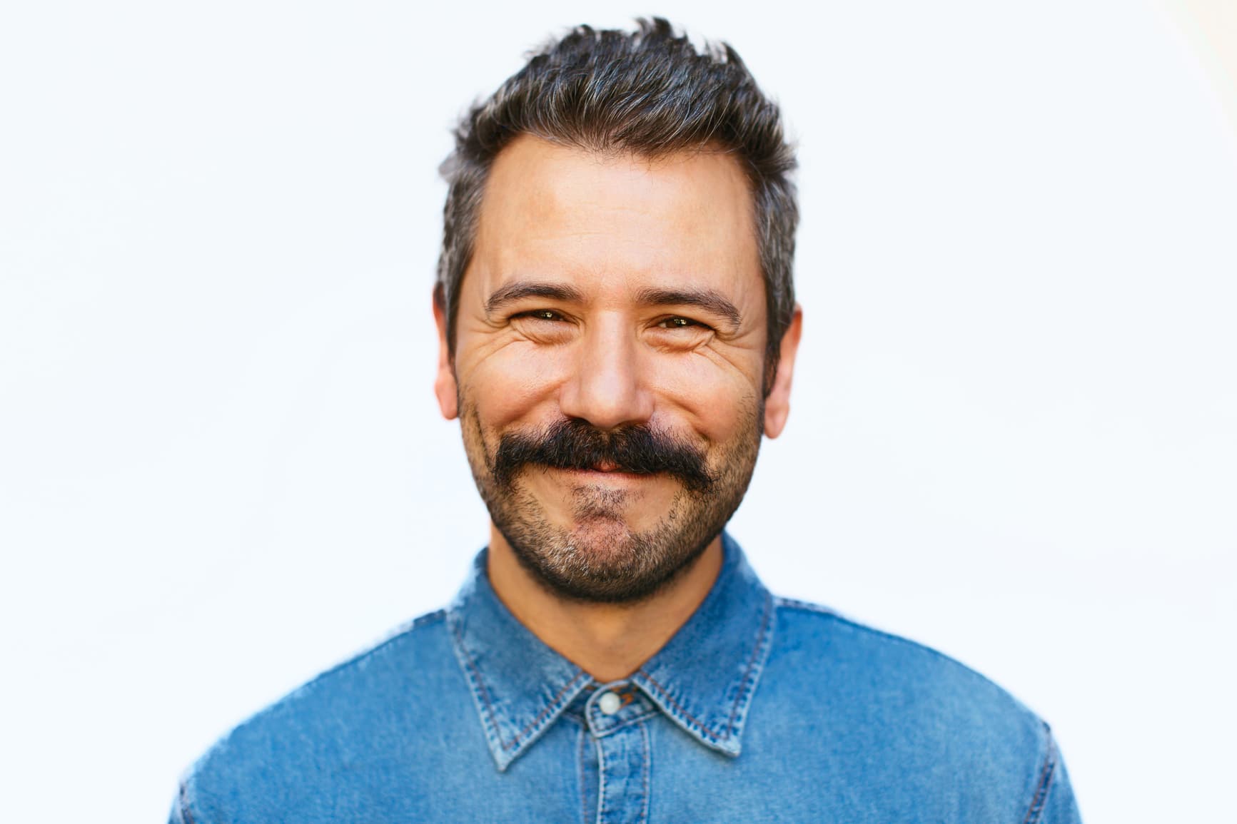 Man in blue denim shirt with beard smiling
