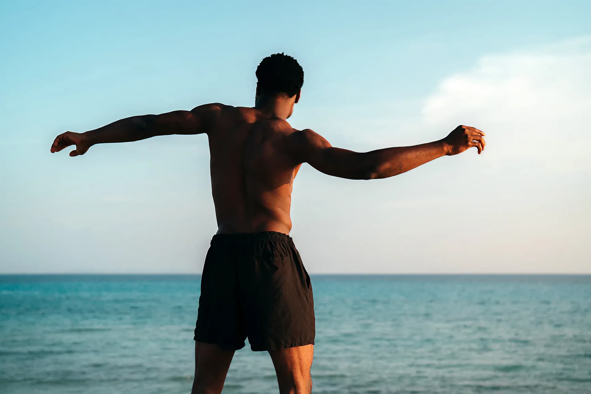Man at the seaside with arms extended, reflecting physical strength, mental clarity, and overall well-being.