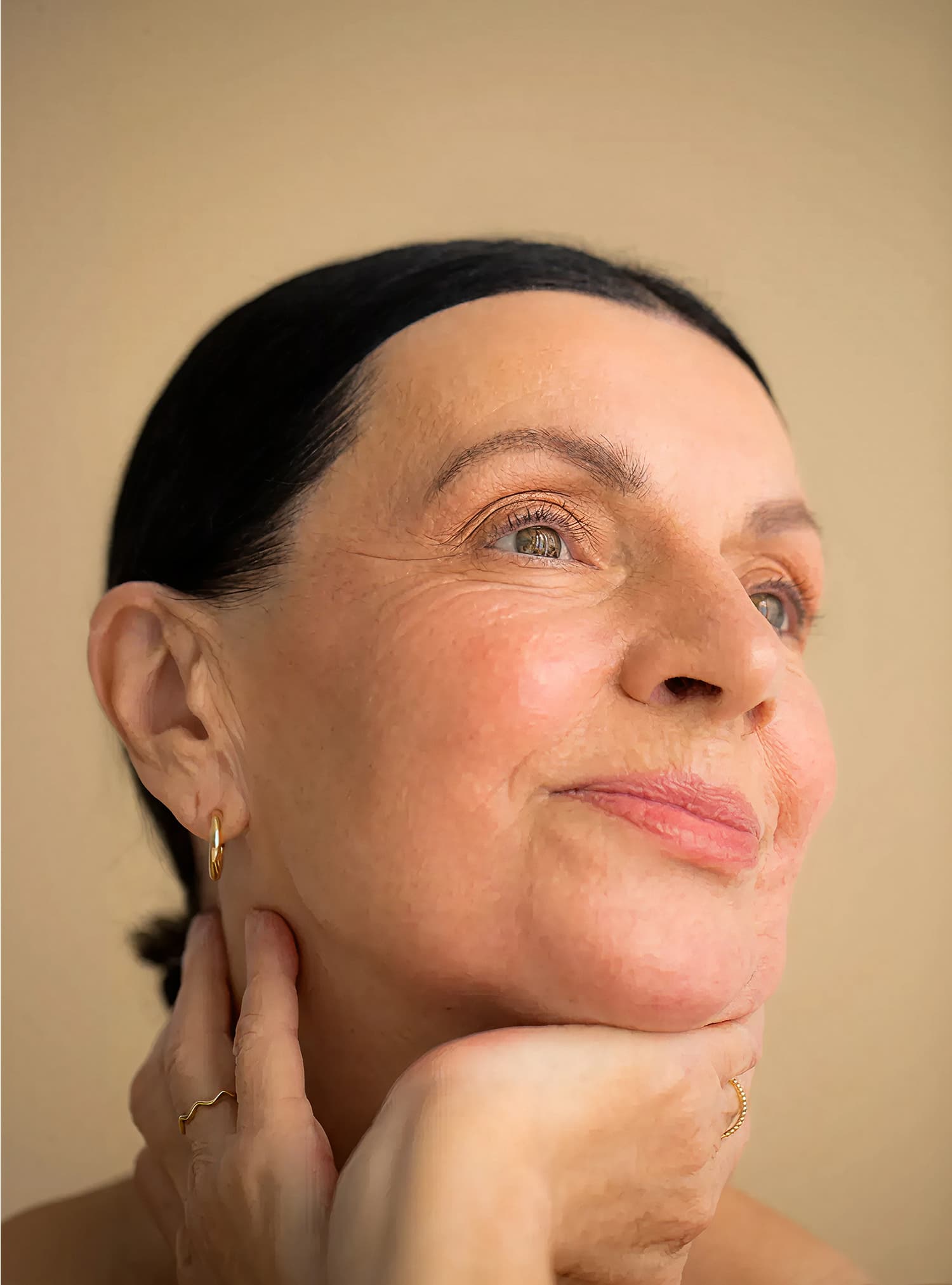 Woman gazes peacefully upward with a serene expression, hands resting gently on her neck, glowing with calm vitality